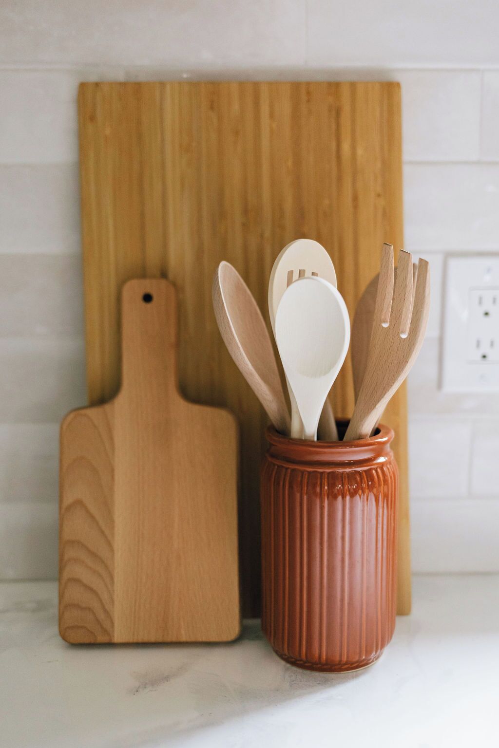 A wooden cutting board and a ceramic container with wooden utensils.