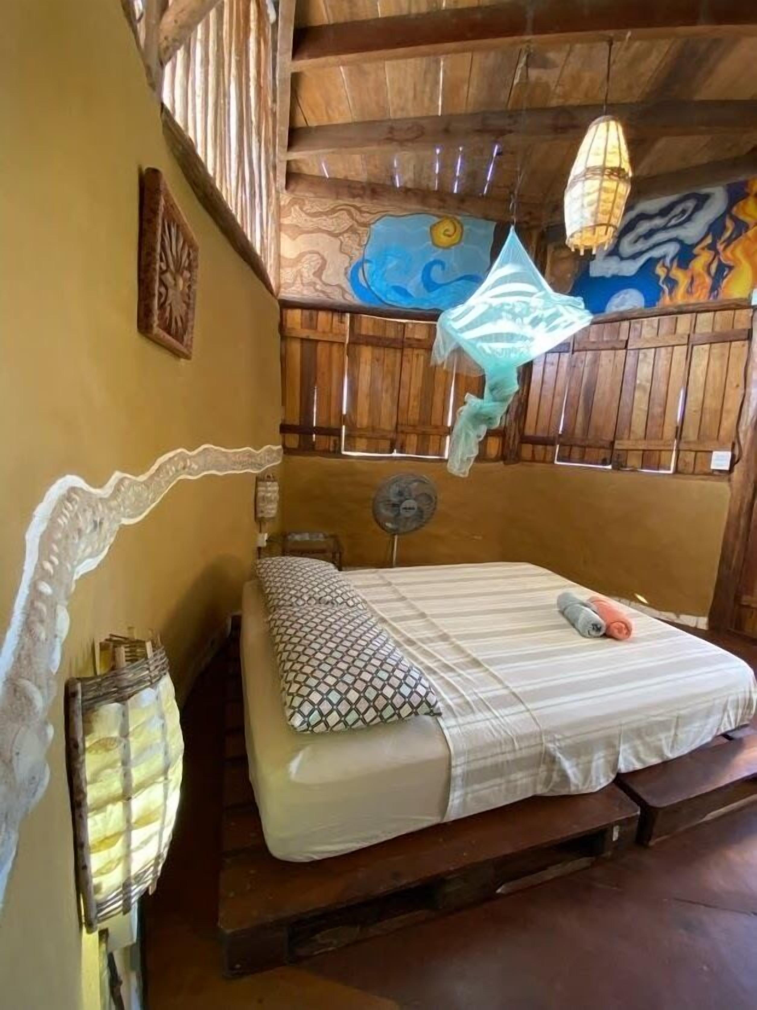 Une chambre avec un lit, un ventilateur et un mur décoratif.