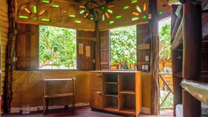 A rustic room with wooden walls, a ceiling fan, and a window with a view of greenery. - Raízes Eco Hostel (Cajueiro da Praia)