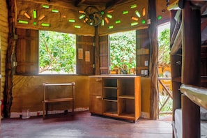 A rustic room with wooden walls, a ceiling fan, and a window with a view of greenery. - Raízes Eco Hostel (Cajueiro da Praia)