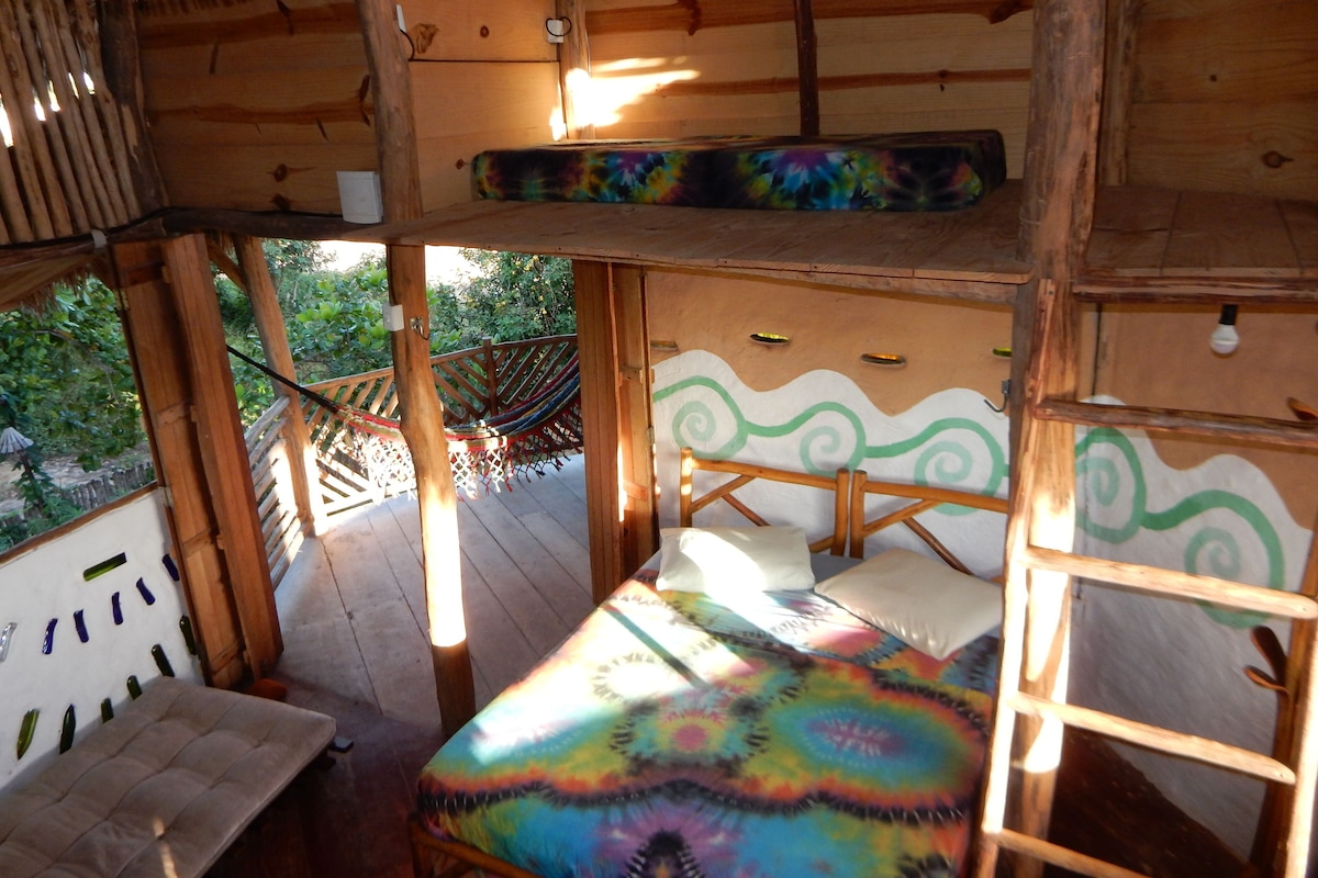 Une cabane en bois avec un lit, un hamac et une vue sur la verdure environnante.