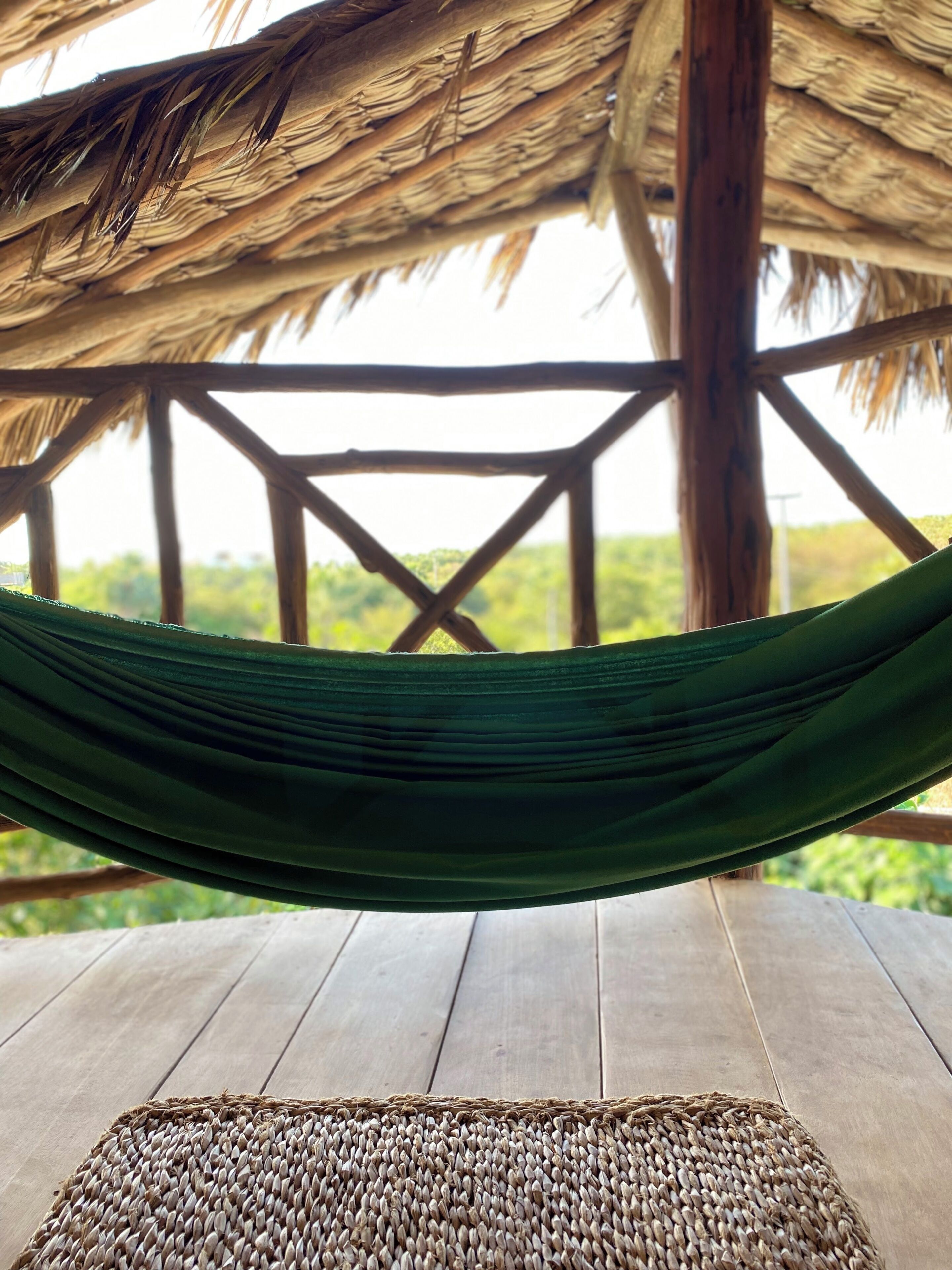 A hammock suspended between wooden beams, with a woven mat on a wooden deck.