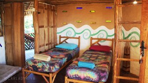 Une pièce rustique en bois, avec deux lits en bois, chacun agrémenté de draps et d’oreillers aux couleurs vives.