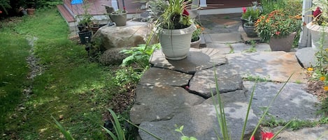 Un jardín con plantas en macetas, un sendero de piedra y una casa con porche.