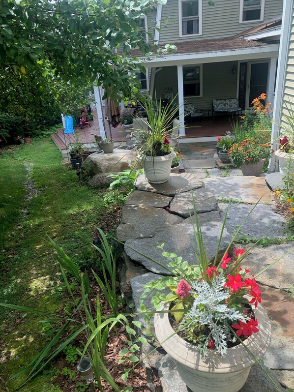 A garden with potted plants, a stone pathway, and a house with a porch.