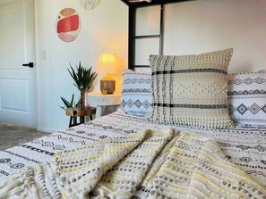 Een bed met beddengoed met een patroon, een bedlampje en een muur met abstracte kunst.