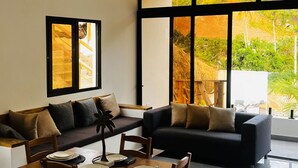 A modern living room with a dining area, large windows, and a view of greenery. -  10 min from the beach!Romantic Spanish apto w/Infinity Pool. (Las Terrenas)