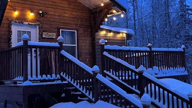A wooden cabin with a covered porch, wooden railings, and a staircase leading up to the entrance. - Cozy pet friendly cabin with stand alone sauna near Willow and Talkeetna Alaska (Willow)