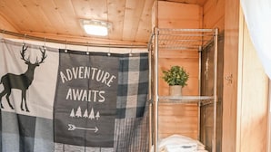 A cozy cabin room with a plaid banner reading "Adventure Awaits" and a bear illustration. There is a shelf with folded towels and a small plant. - Cozy pet friendly cabin with stand alone sauna near Willow and Talkeetna Alaska (Willow)