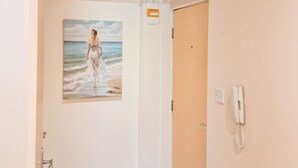 Un couloir orné d’un tableau représentant une femme sur la plage, avec une porte en bois et un téléphone fixé au mur.