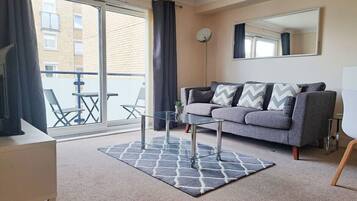 A modern living room with a grey sofa, a glass coffee table, and a patterned rug.