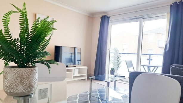Un salon moderne avec un canapé, une table basse en verre, une fougère en pot et un téléviseur posé sur un meuble.