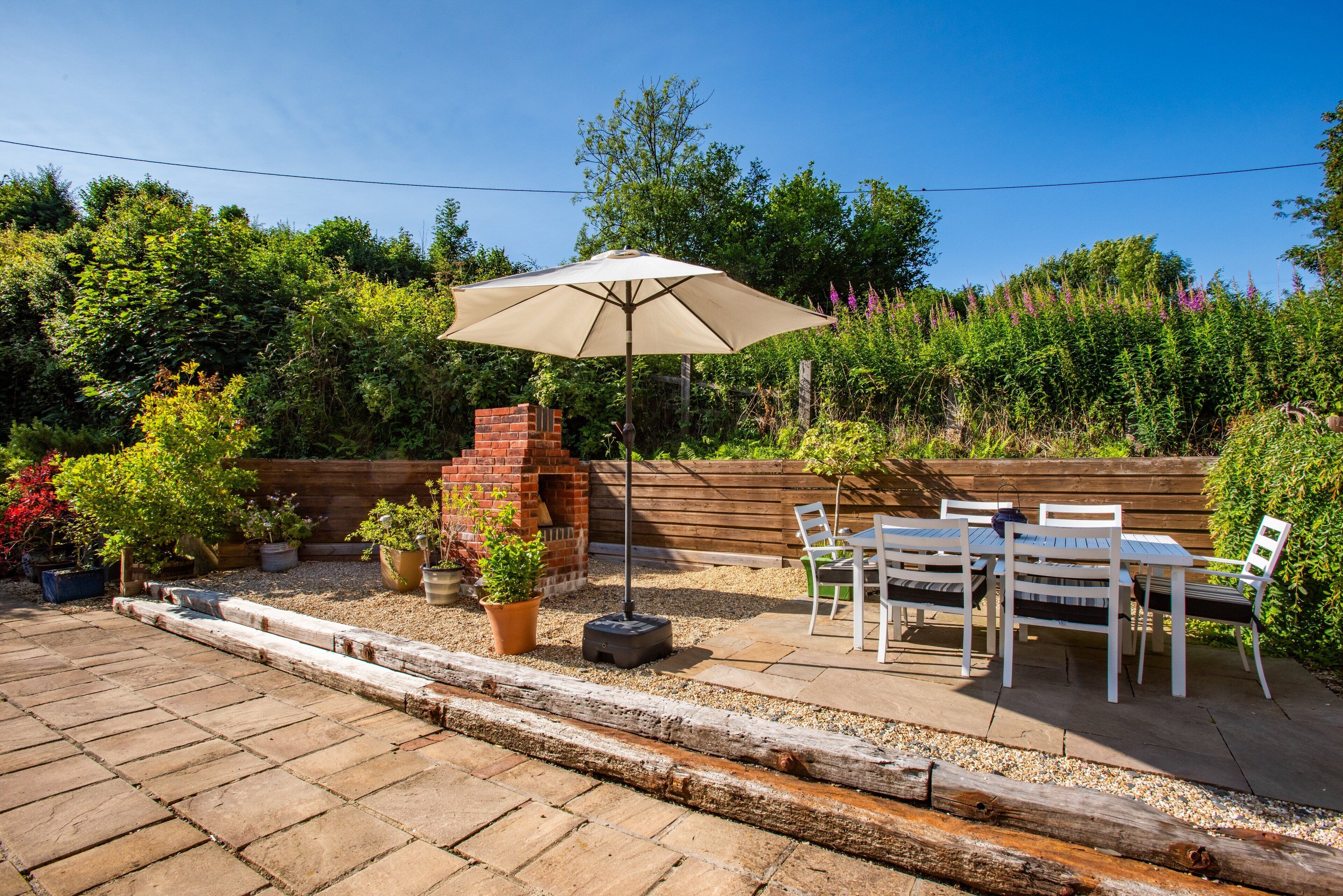An outdoor patio with a brick fire pit, a table and chairs, and a large umbrella.