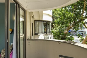 A balcony with a curved railing, a view of a street with a bus stop, and a tree.