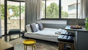 A compact hotel room with a bed, a small kitchenette, a dining area, and a view of the outside. - Turquoise Chic Dizengoff CTR by SeaNRent (Tel Aviv)