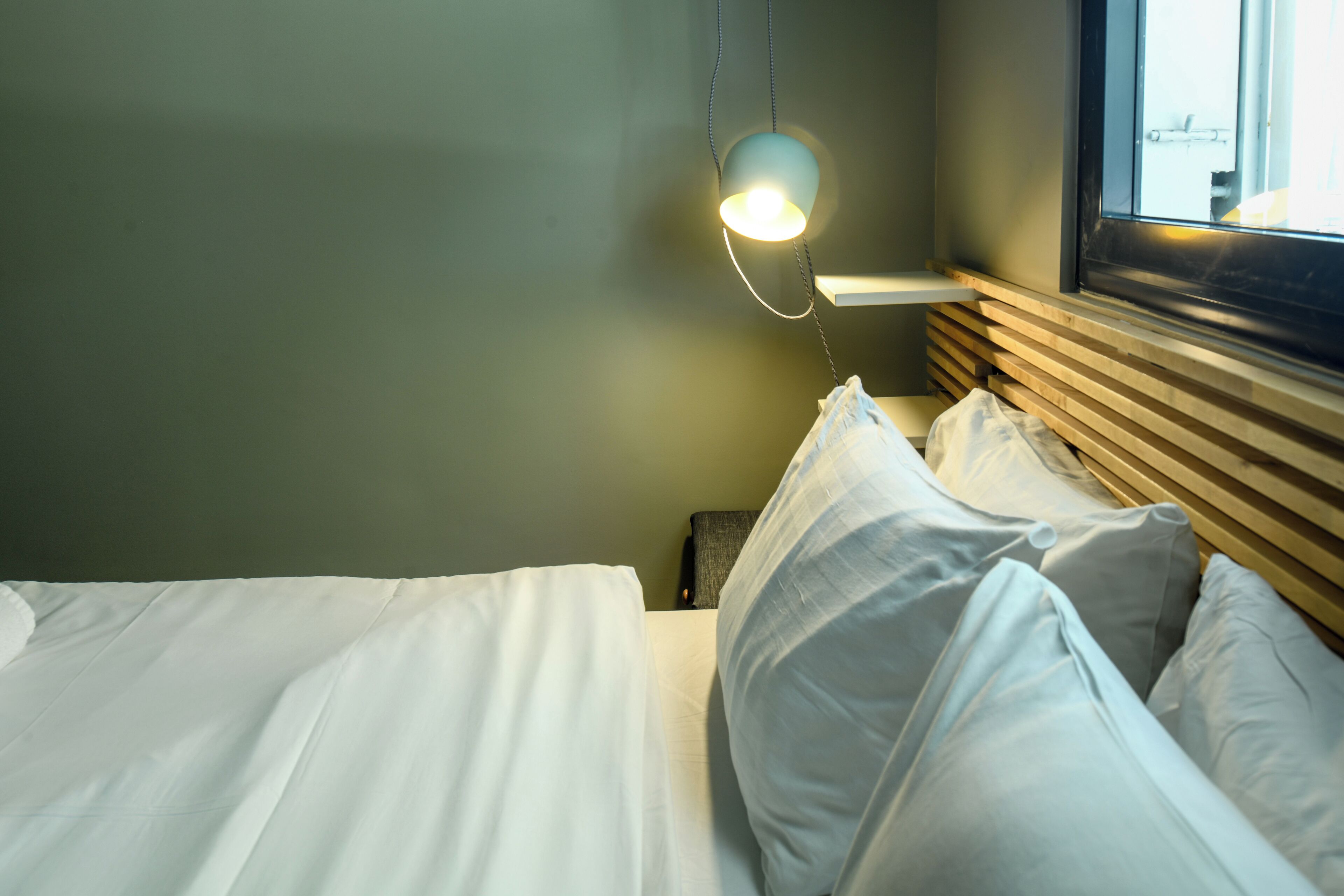 Ein ordentlich bezogenes Bett mit weißen Leinen und ein Nachttisch mit Lampe.