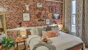 A cozy bedroom with a brick wall, a bed with a fluffy pillow, a bedside table with a lamp, and a world map on the wall. - 2 Bdrm Sits on Riverwalk (San Antonio)