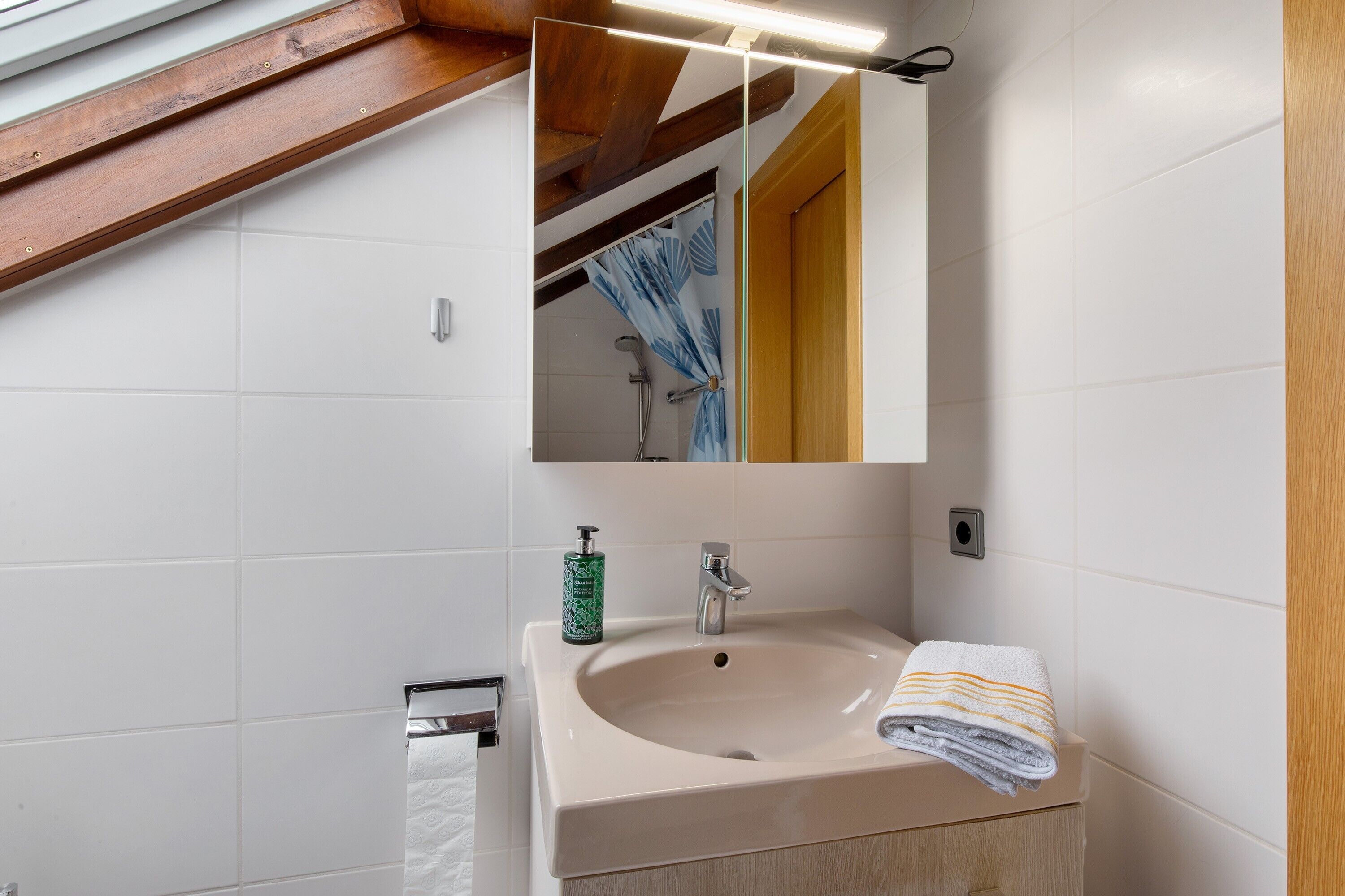 A bathroom with a sink, mirror, towel, and a bottle of soap.