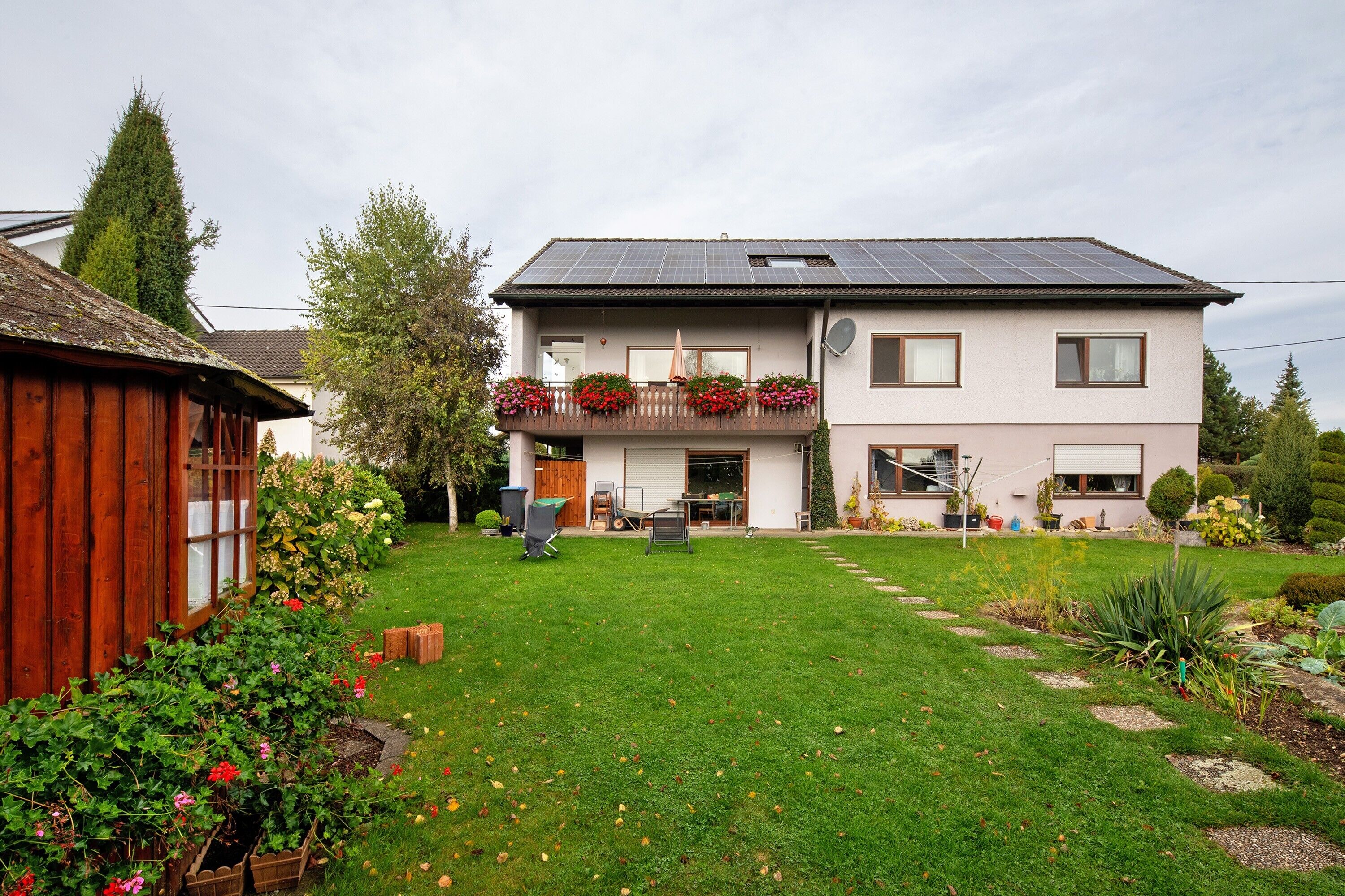 A two-story house with a balcony, solar panels, and a well-maintained garden.