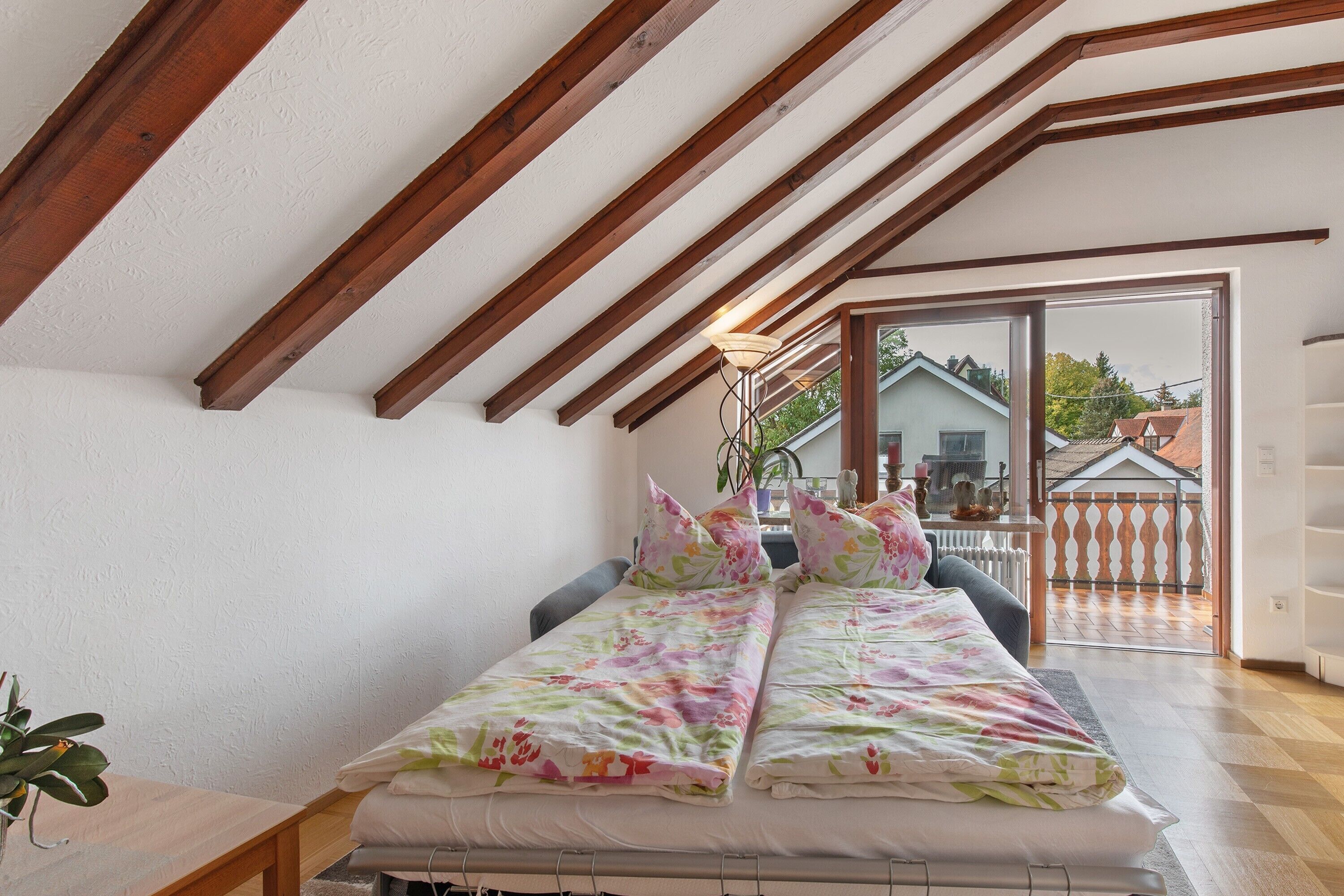 Un dormitorio con cama, vigas de madera, una ventana y vistas al exterior.