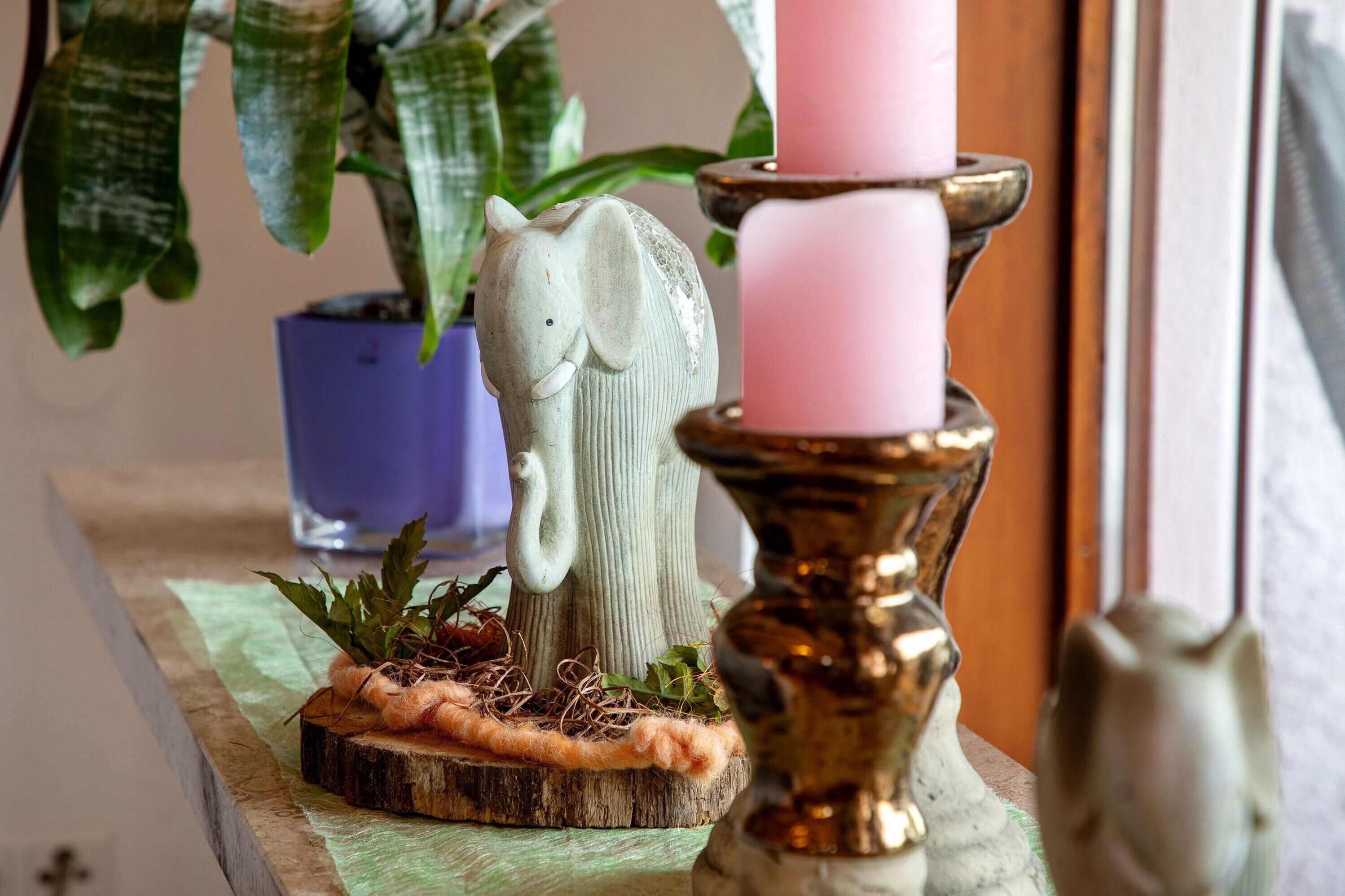A decorative elephant figurine, a pink candle, and a brass candlestick on a wooden surface.
