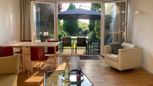 Een moderne woonkamer met een eethoek, een bank en een glazen tafel met een fles en een doos.