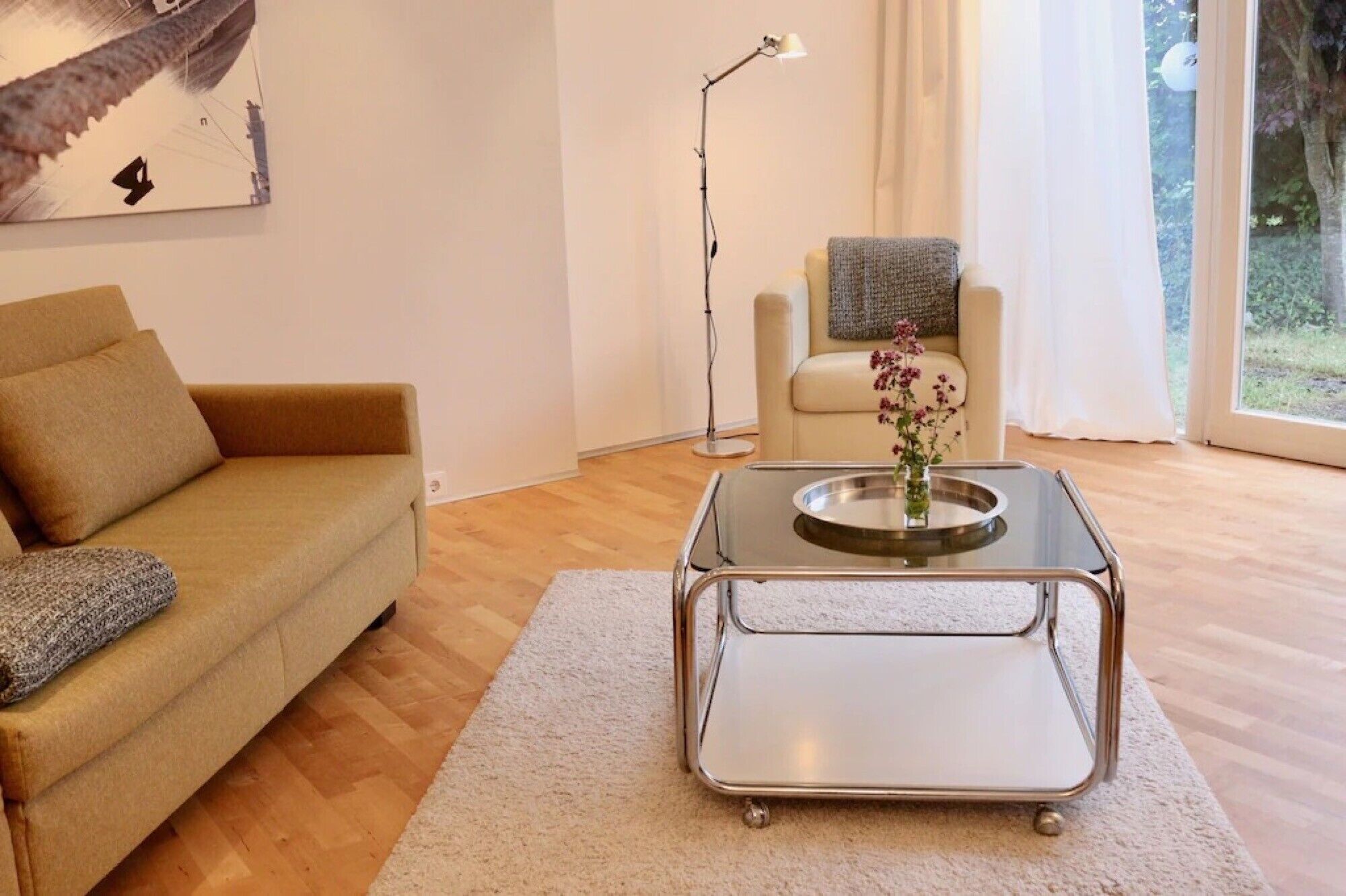 Un salon avec un canapé, une table basse ornée d’un vase, un lampadaire et une vue par la fenêtre.