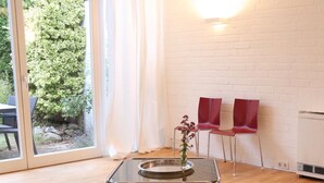 Een kamer met een glazen tafel, twee rode stoelen, een witte bakstenen muur en uitzicht op groen buiten.