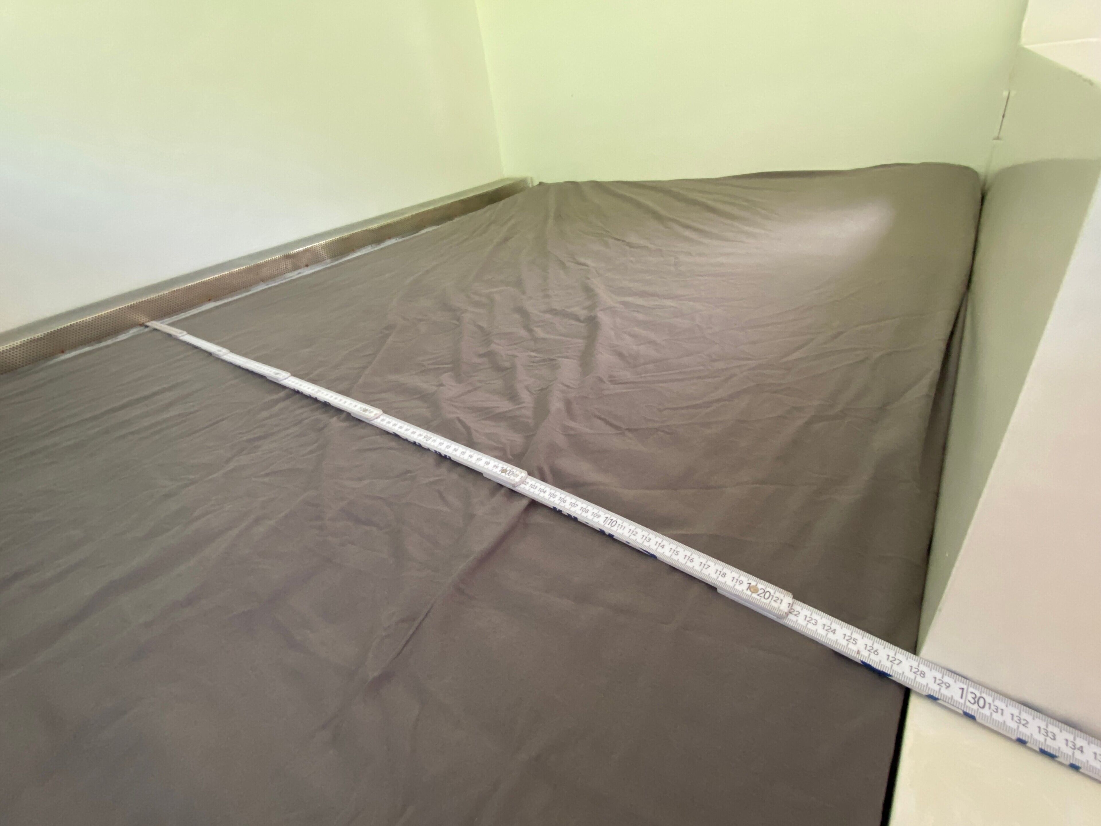 A room with a mattress on the floor, a measuring tape across it, and a partial view of a wall.