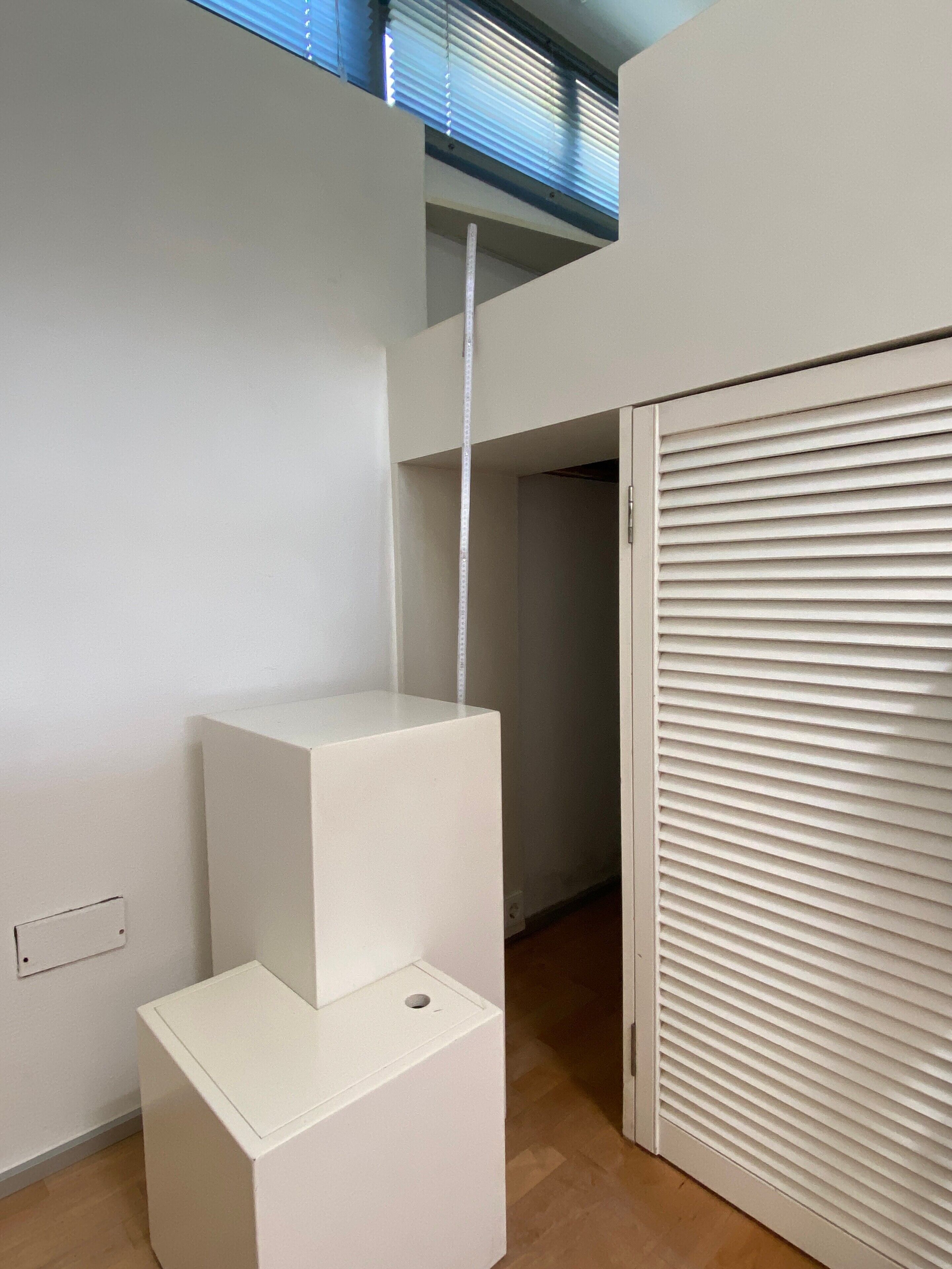 Une pièce avec une armoire blanche, un banc blanc et une fenêtre avec des stores.
