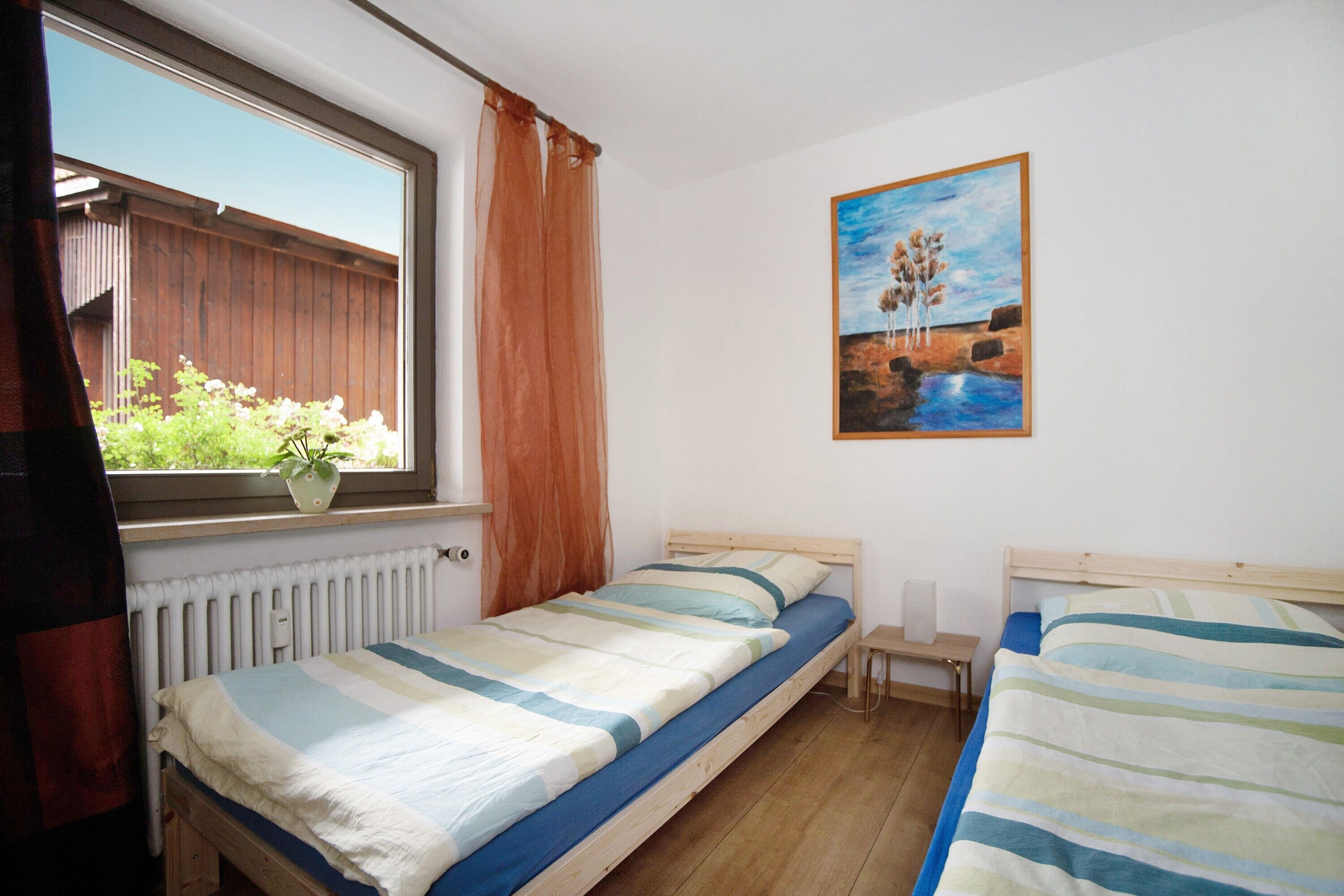 Ein Schlafzimmer mit zwei Einzelbetten, einem Fenster mit Blick auf Grünflächen, einem Heizkörper und einem Bild an der Wand.
