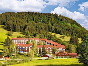 A hotel with multiple buildings, a green landscape, and a forested hill in the background.