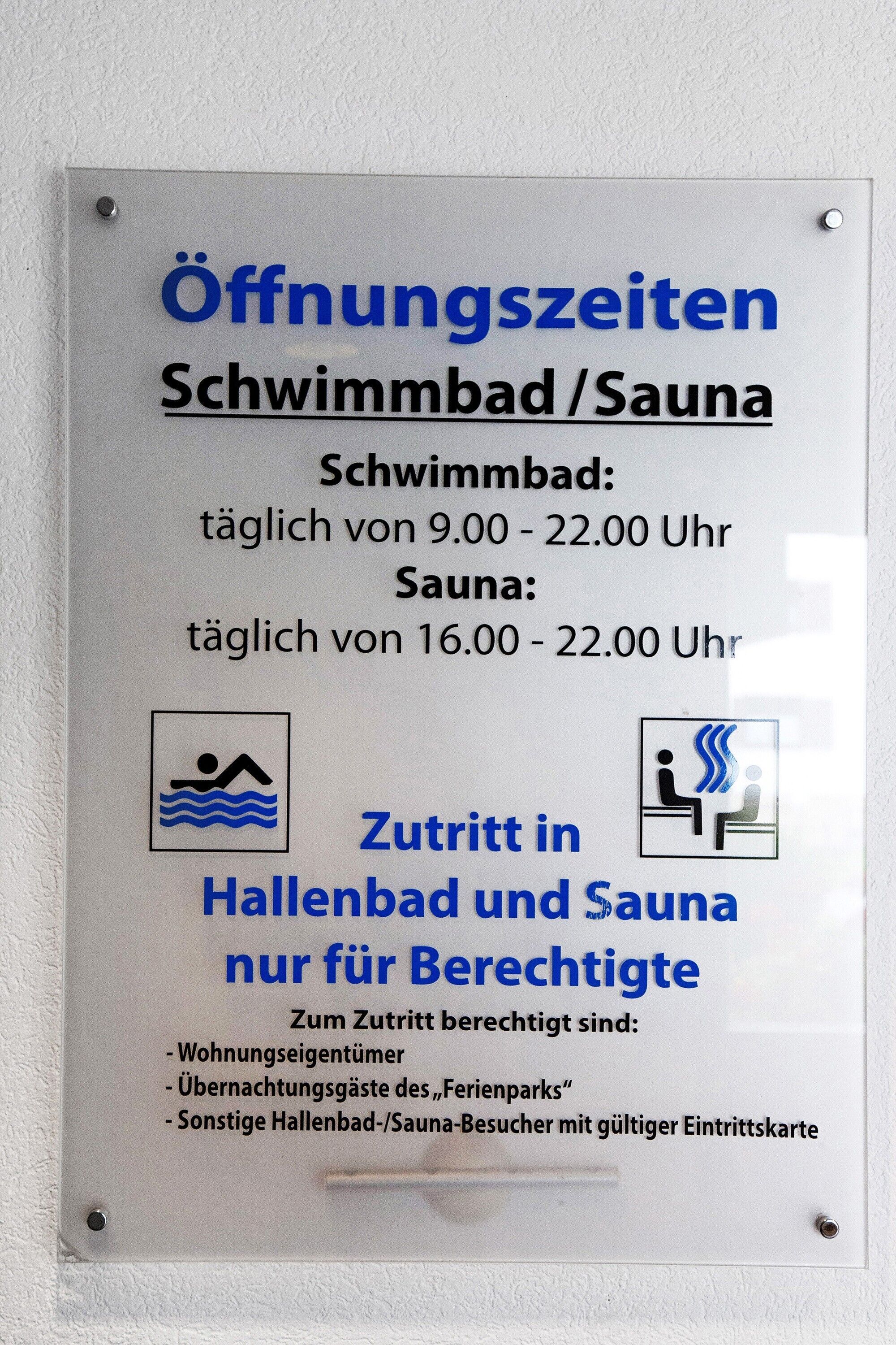 Een bord met de openingstijden van een zwembad en sauna, met tijden voor beide voorzieningen.