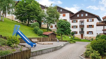 Un parque infantil con un tobogán azul, un banco de madera y un edificio pequeño.
