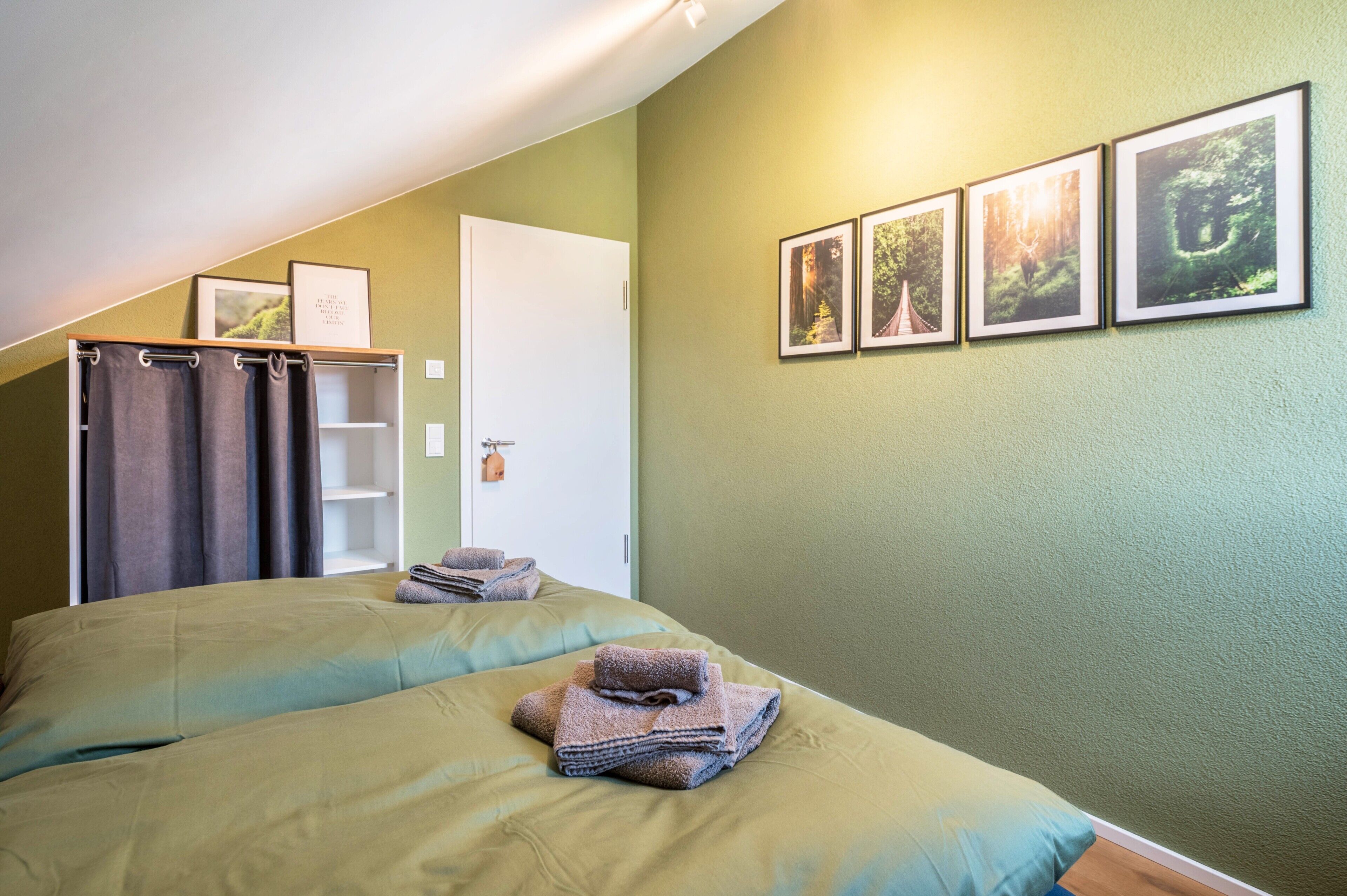 Ein Hotelzimmer mit zwei Betten, einem Kleiderschrank, einer Tür und vier gerahmten Bildern an der Wand.