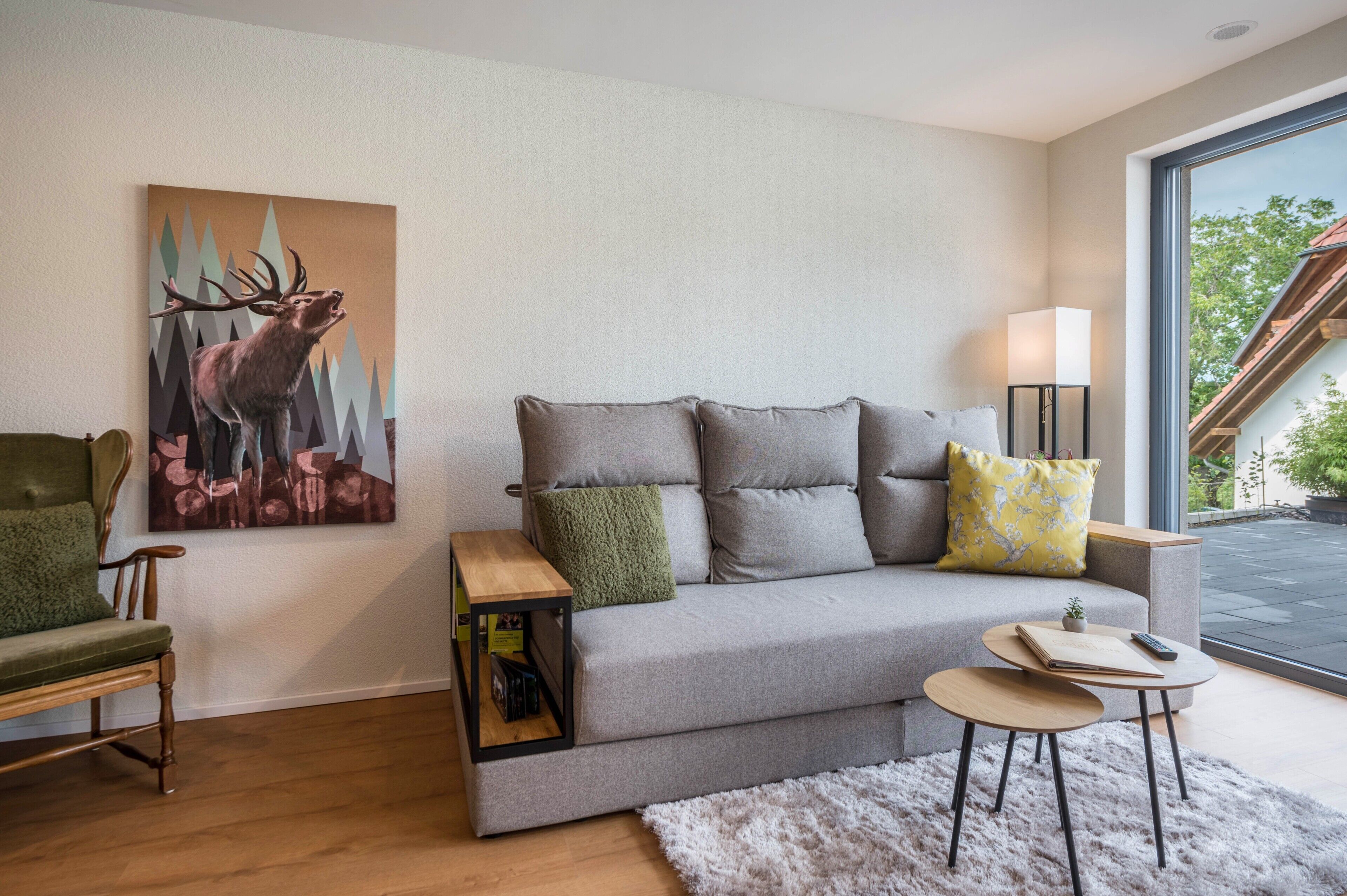 Ein modernes Wohnzimmer mit einem grauen Sofa, einem Holztisch, einem grünen Sessel und einem Bild von einem Reh.