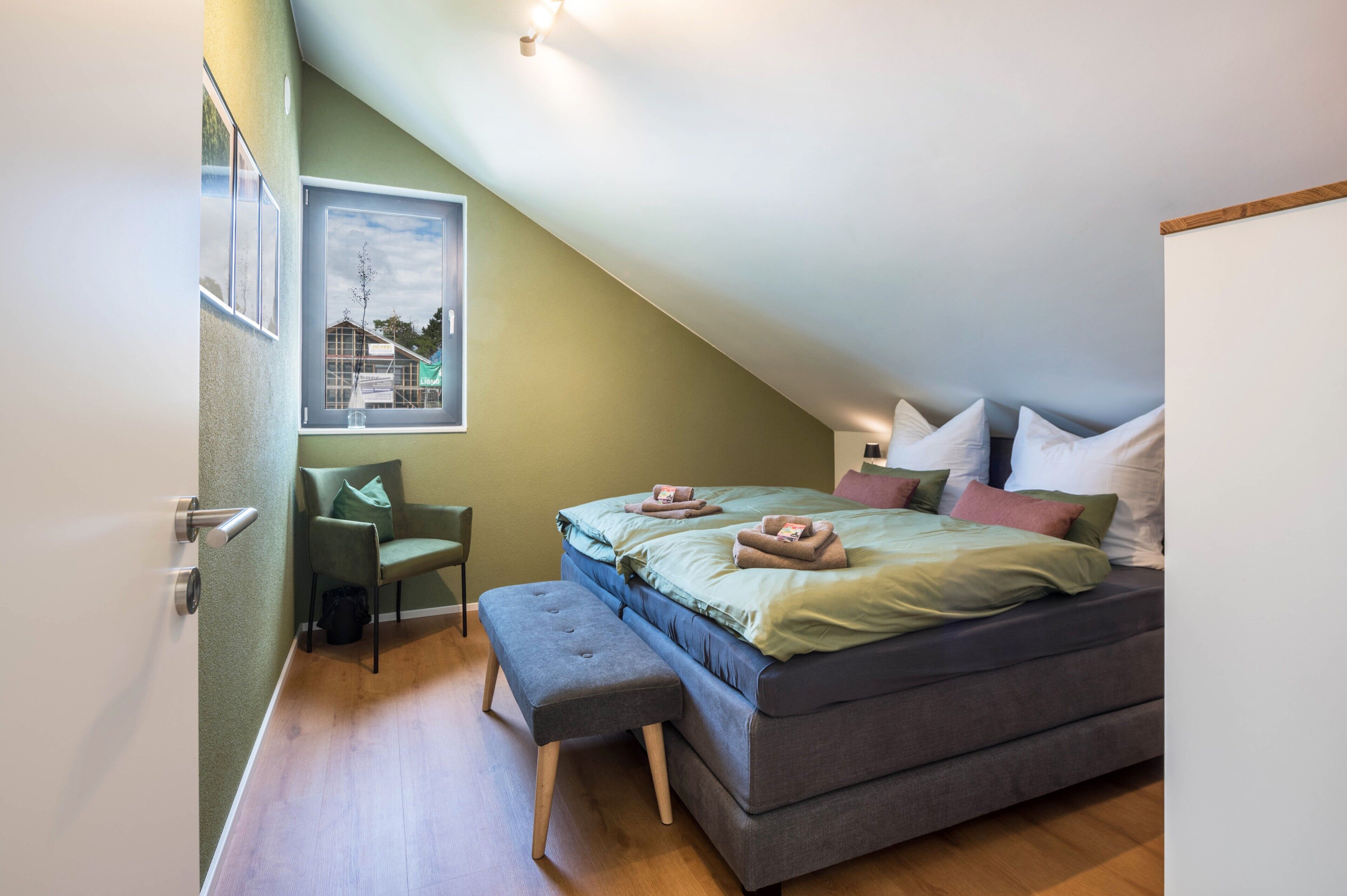 Un dormitorio con cama, una silla, un banco y un cuadro colgado en la pared.
