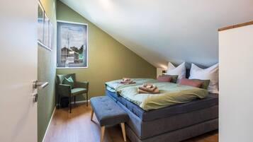 Un dormitorio con cama, una silla, un banco y un cuadro colgado en la pared.