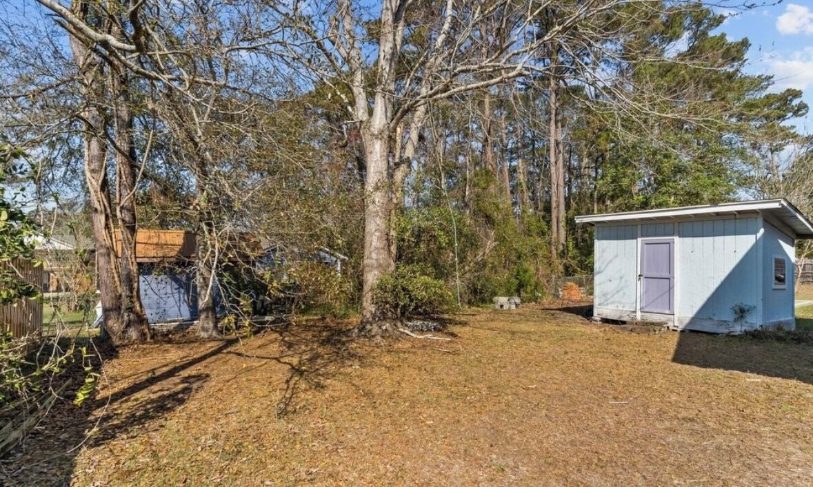 A small, single-story building with a light blue exterior and a dark blue door, surrounded by trees and a grassy yard.