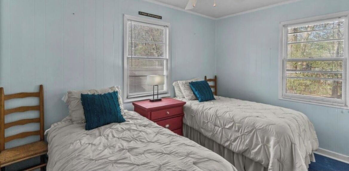 A bedroom with two beds, a nightstand, and a window with blinds.