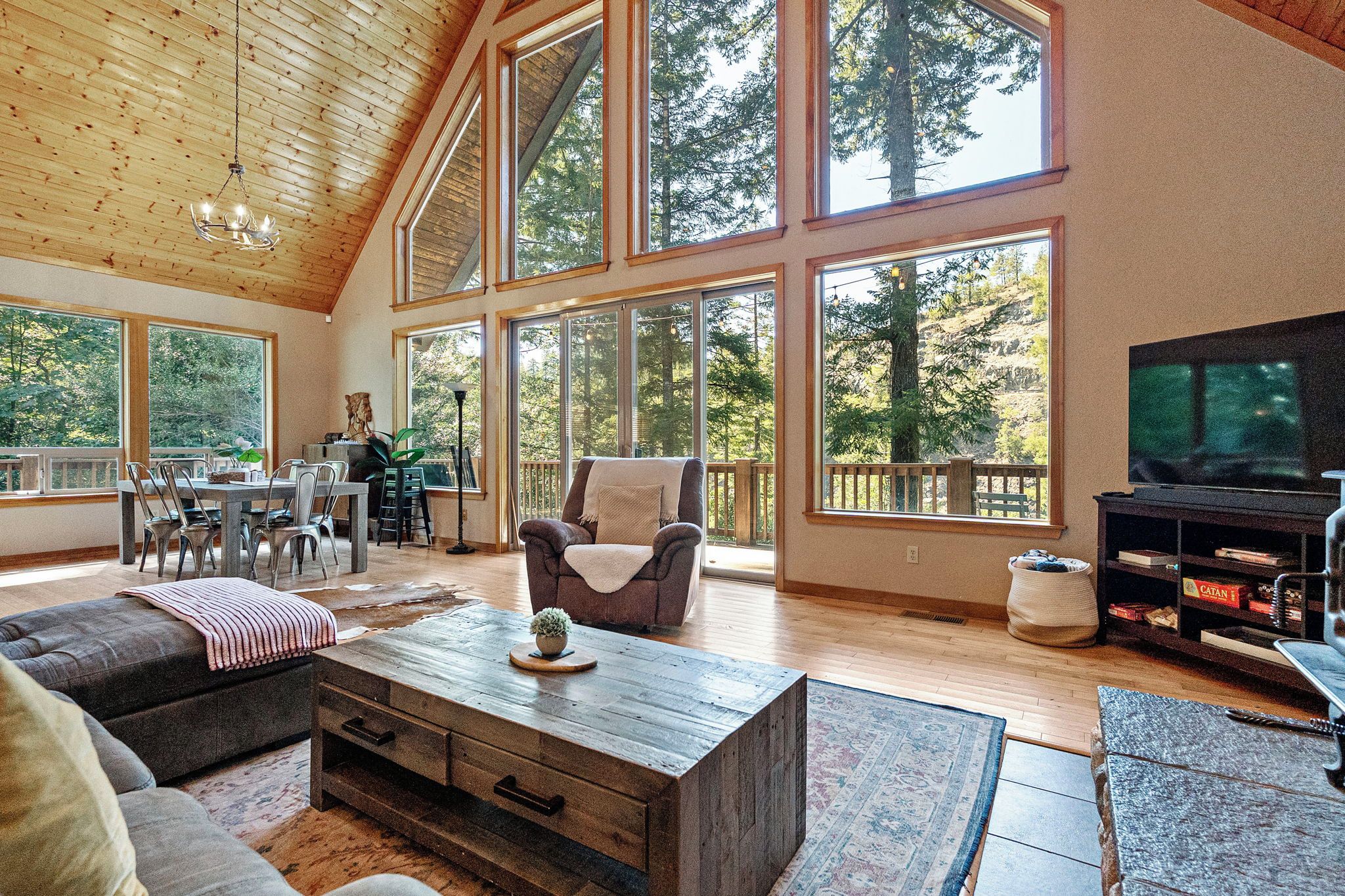 A spacious living room with a high ceiling, large windows, a fireplace, and a television.