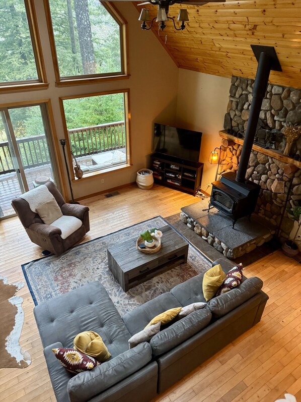 A cozy living room with a stone fireplace, a large TV, and a comfortable seating area with a sofa and armchair.