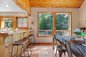 Un interior de madera con área de cocina, taburetes de bar y una mesa de comedor con sillas.
