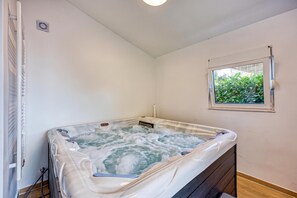 A hot tub in a room with a window, a radiator, and a door.