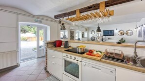 Une cuisine moderne avec un plafond orné de poutres en bois, un four encastré et un évier surmonté d’un porte-bouteilles.