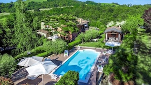 A large swimming pool with lounge chairs and umbrellas, surrounded by lush greenery and a hillside view. - Villa Banci 8 Emma Villas (Urbino)