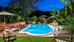 Une piscine rectangulaire avec une terrasse carrelée, entourée de chaises longues et de parasols.
