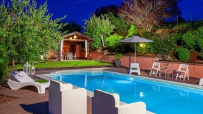 Une piscine avec des chaises longues, un espace de détente couvert et un jardin bien entretenu.
