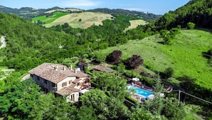 A villa with a swimming pool surrounded by lush greenery and hills in the background. - Villa Banci 8 Emma Villas (Urbino)