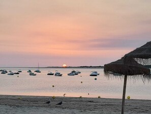 A beach with boats and a thatched umbrella.